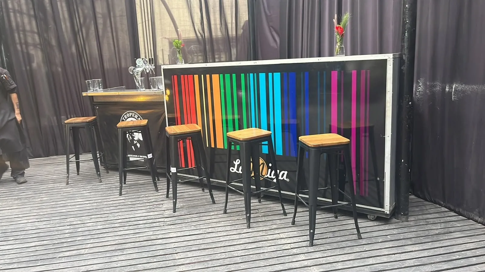 Barra de La Miga en la terraza, con el logo iluminado sobre franjas de colores y piso de madera