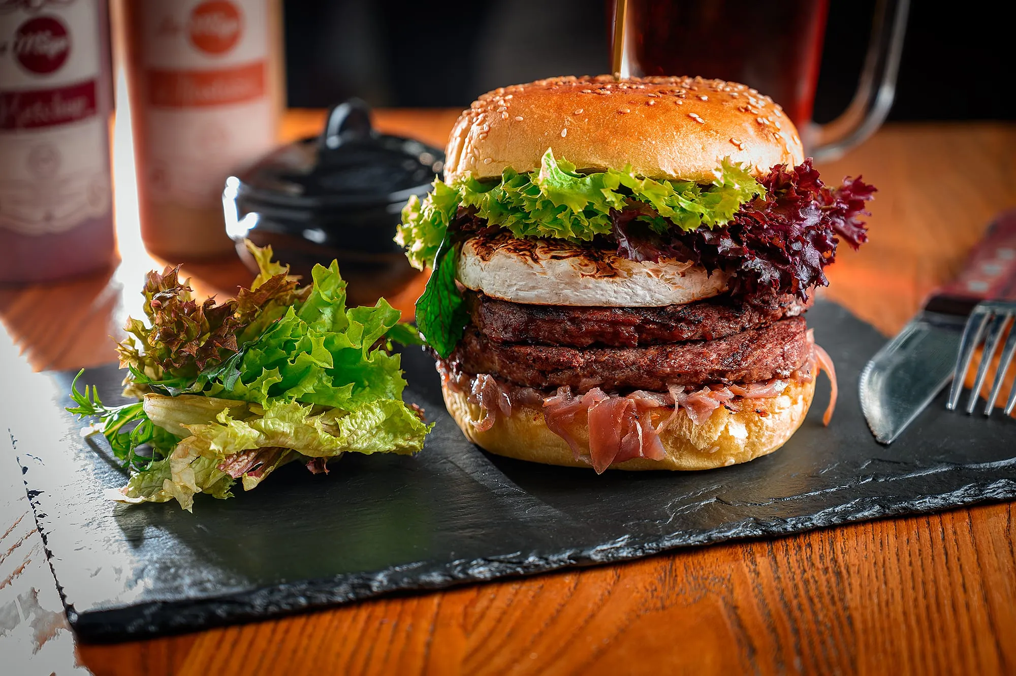 Hamburguesa doble con aro de cebolla, tocino y lechuga, servida sobre una pizarra de piedra