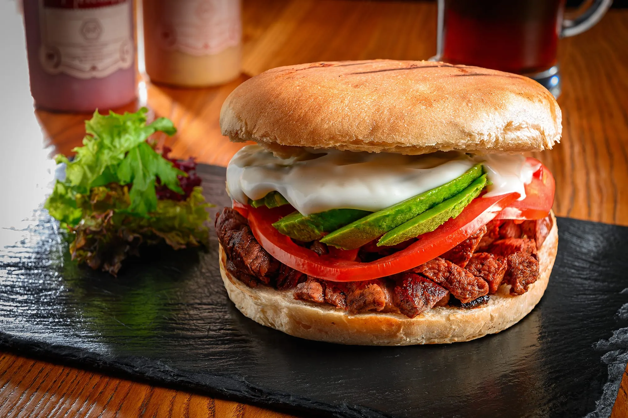 Sánguche de carne mechada con tomate, palta y mayonesa sobre una pizarra de piedra