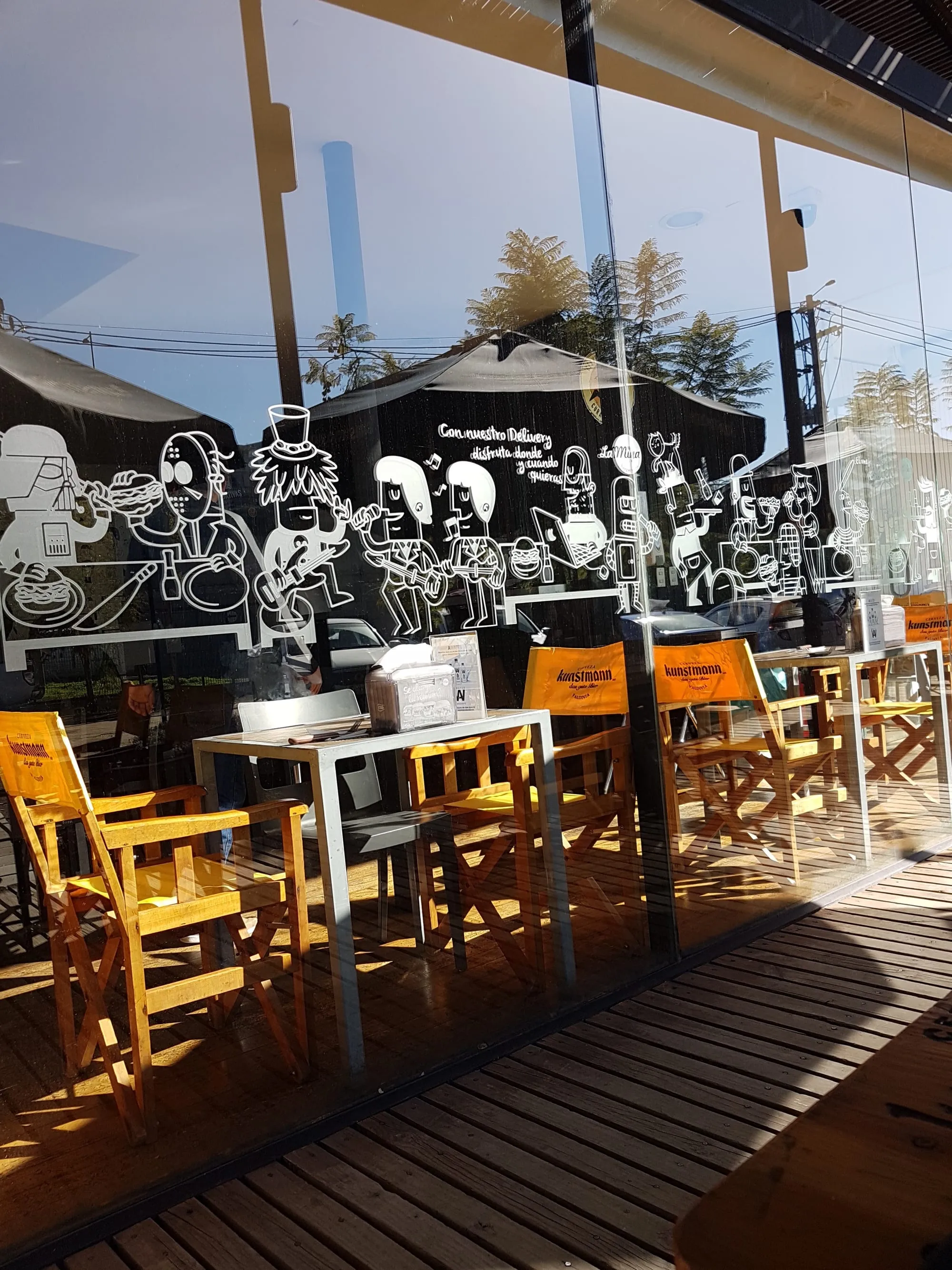 Terraza techada de La Miga con sillas amarillas y el mural de personajes dibujado sobre la pared negra