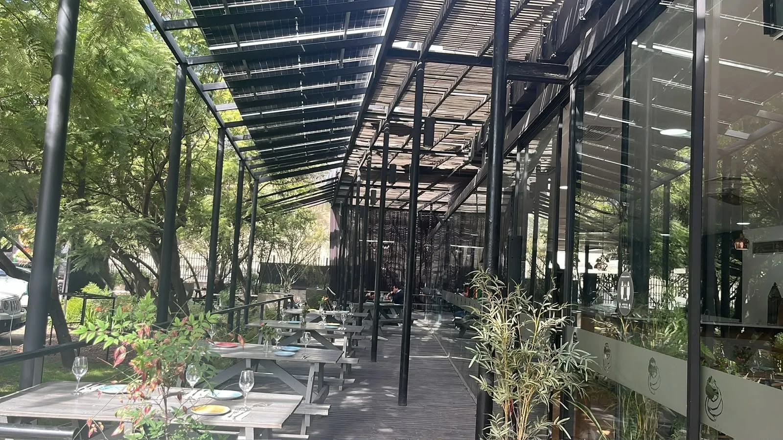 Terraza techada de La Miga de día, con la estructura negra abierta hacia los árboles